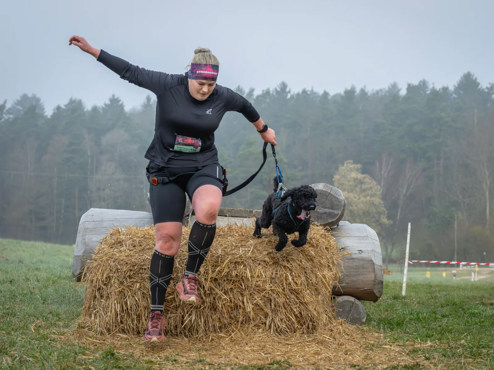 Canicross Mensch-Hund-Team springt von Strohballen