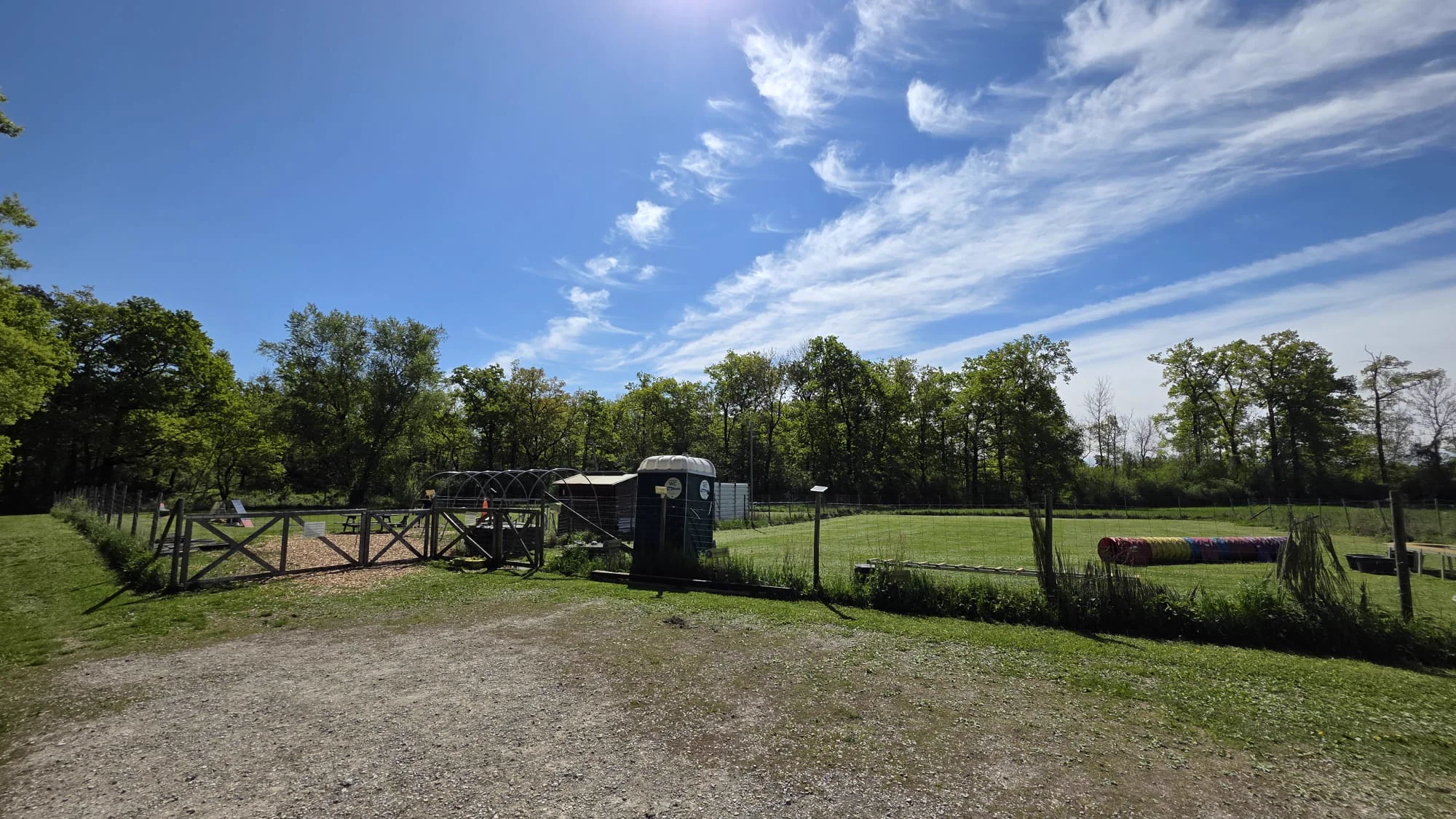 Eingangsbereich des Dogrelation Hundeplatzes in Ennsdorf mit Tor, Vereinshütte und Agility-Geräten