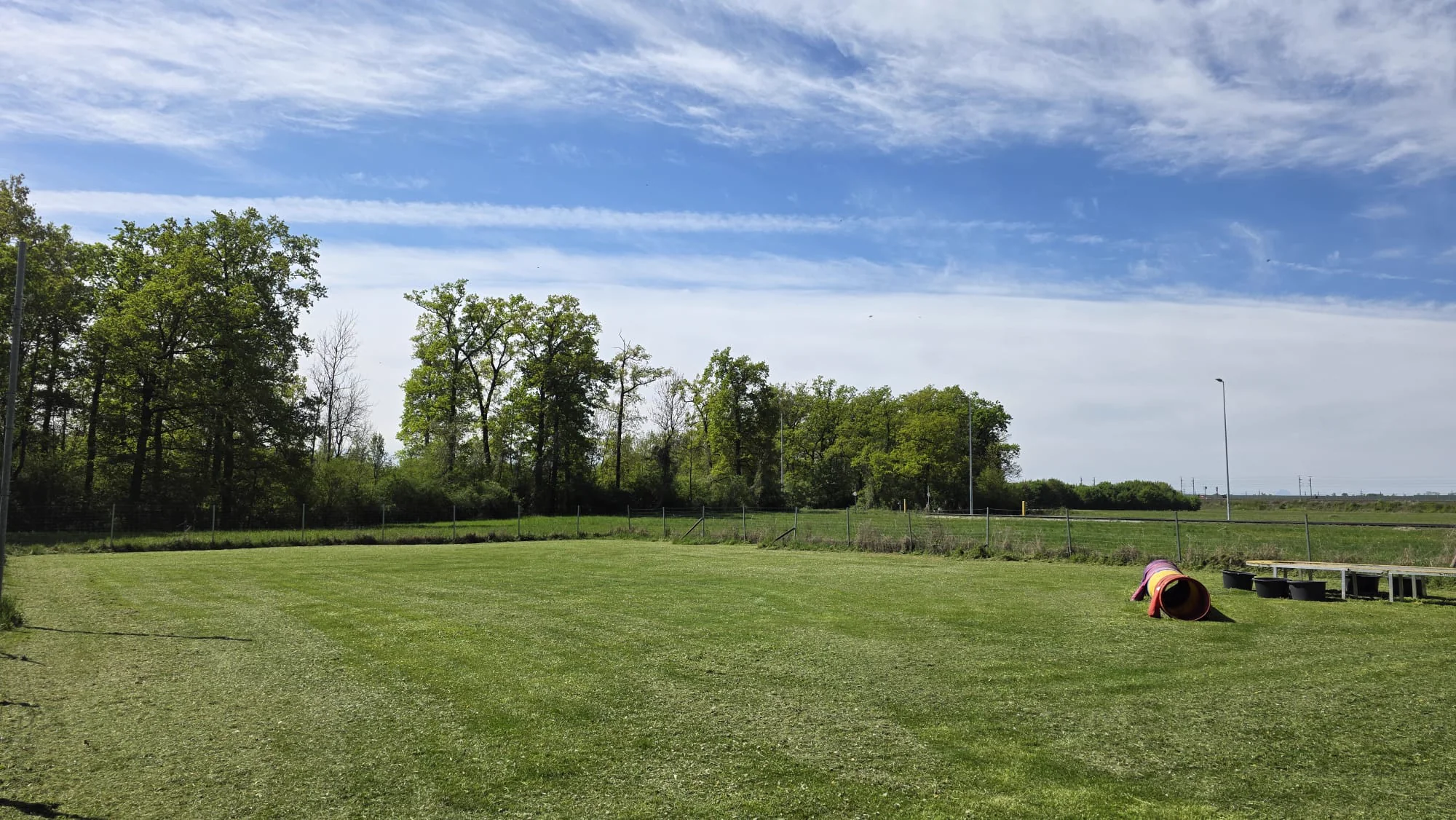 Großzügiges Trainingsgelände des Dogrelation Hundeplatzes in Ennsdorf mit Agility-Tunnel und weiter Wiese unter blauem Himmel