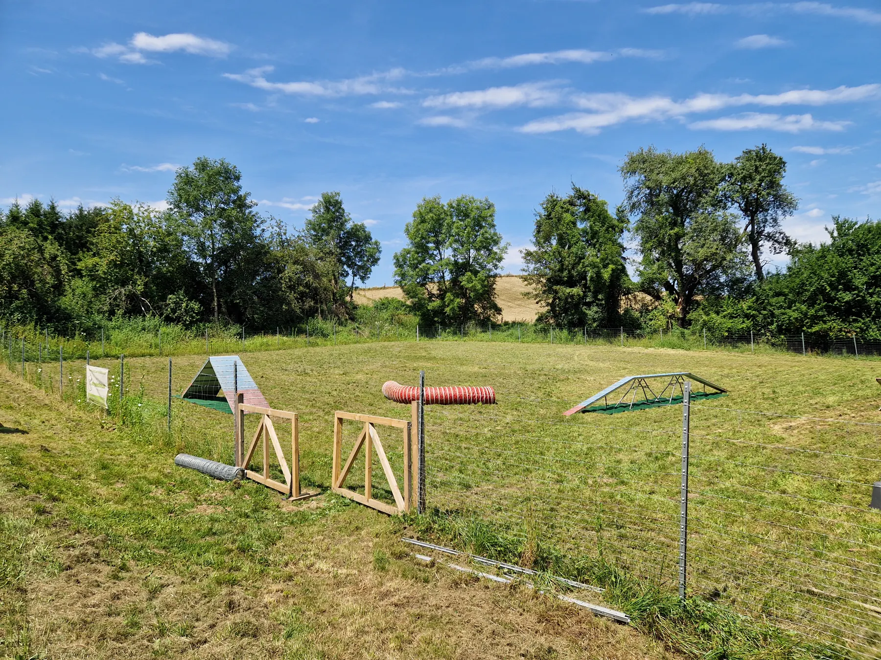 Übersicht des Dogrelation Hundeplatzes in Wolfern mit Agility-Tunnel und Doppelhürde unter blauem Himmel