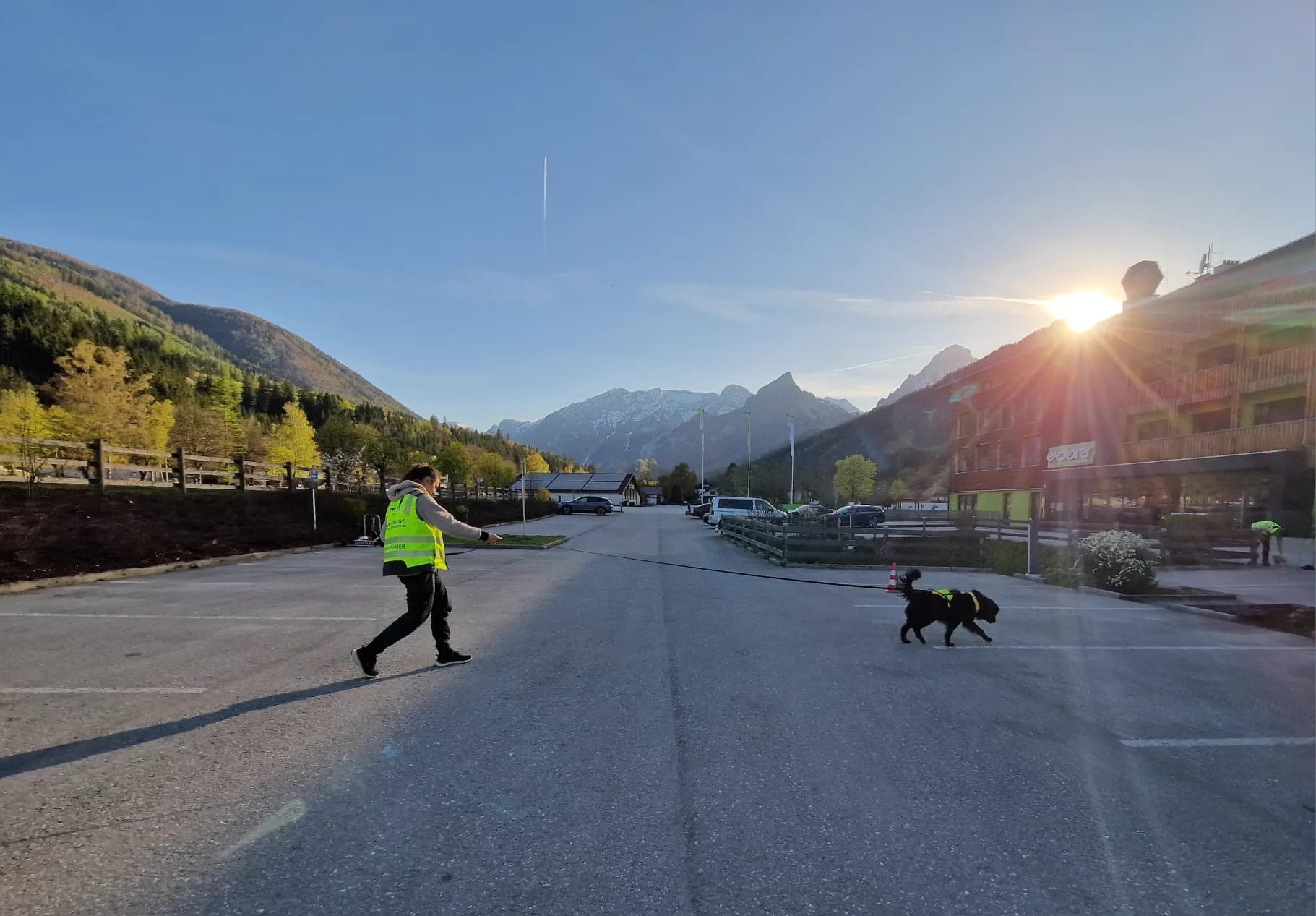 Mantrailing im Sonnenaufgang – Hundeführerin und Hund queren Parkplatz vor Bergpanorama – Dogrelation (Bild 18)